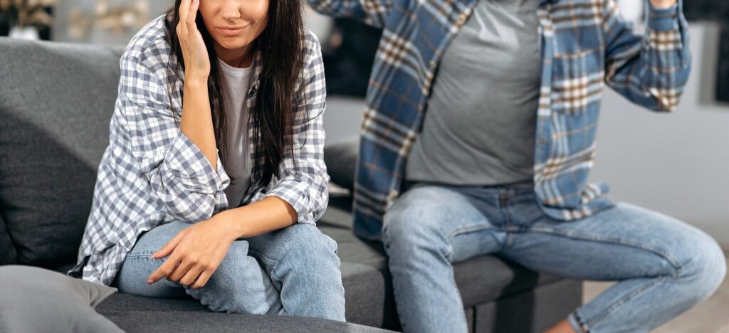 A close up of a couple appearing to argue while sitting on opposite sides of a couch. This could represent the stress of cultural differences that EFT couples therapy in Hermosa Beach, CA can help you overcome. Learn more about emotionally focused therapy in Hermosa Beach, CA and how a couples therapist can help today. 
