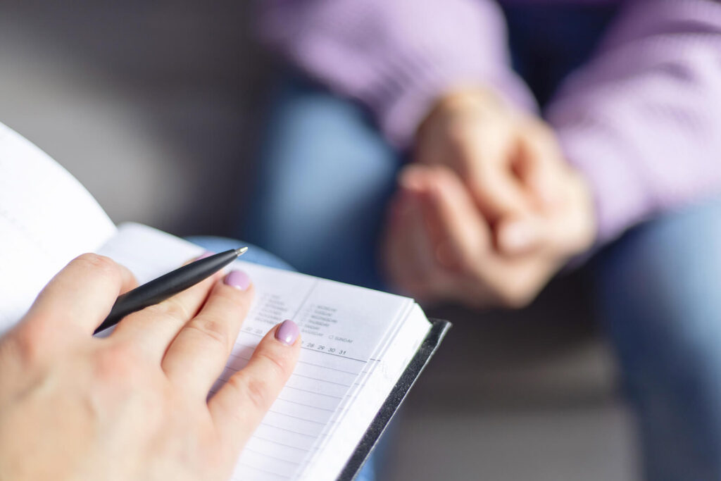 A close up of a person’s hand resting on a notepad while sitting across from a person listening intently. This could represent the support of an EFT couples therapist in Hermosa Beach, CA can offer via couples therapy Hermosa Beach. Search for online therapy in Hermosa Beach, CA today.
