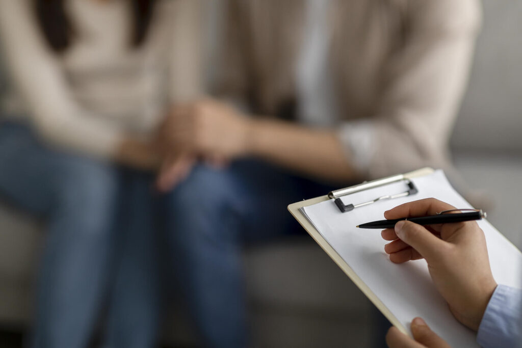 A close up of a person with a clipboard taking notes while sitting across from a couple holding hands and sitting on a couch. Learn how couples therapy in Hermosa Beach, CA can help cultivate deeper bonds. Search for interracial relationships in South Bay, CA to learn more about multicultural couple therapy in Palos Verdes and across the state. 
