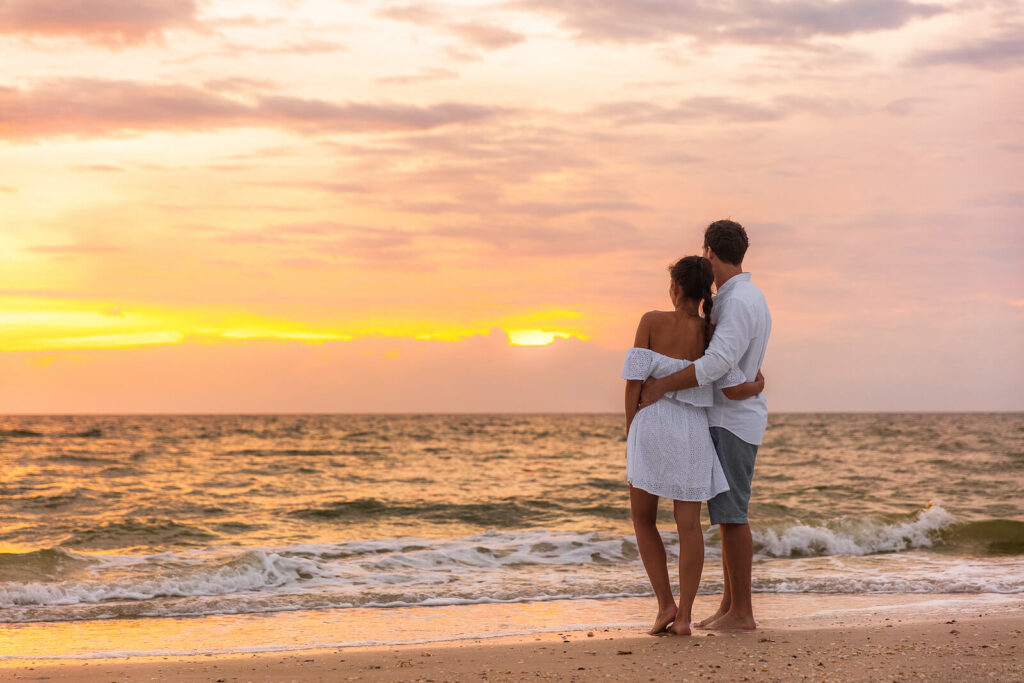 A couple embrace while standing on the shore of an evening beach. Learn more about multicultural marriage counseling and local activities in Hermosa Beach. Contact a couples therapist in Hermosa Beach, CA for more support with couples therapy hermosa beach. 
